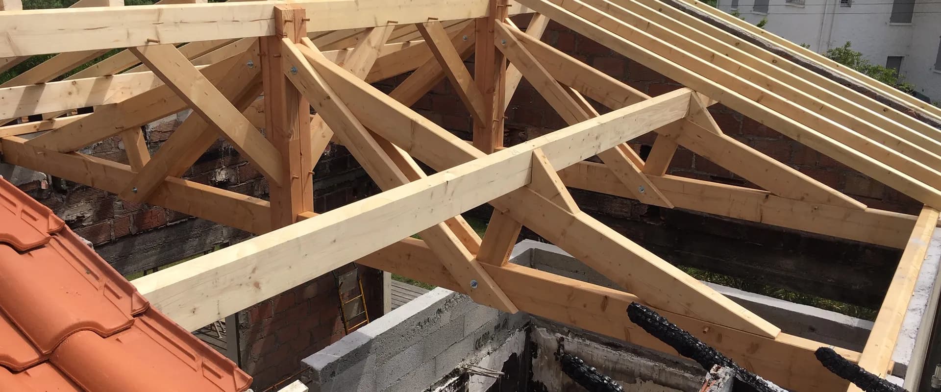 Fermes de charpente neuves posées sur une maison sinistrée, bois carbonisés visibles sous la structure
