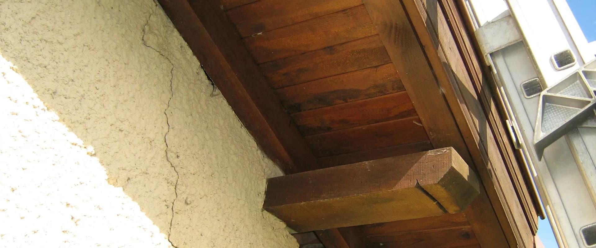 Fissure verticale dans l'enduit d'un pignon, sous l'avant-toit d'une maison ancienne