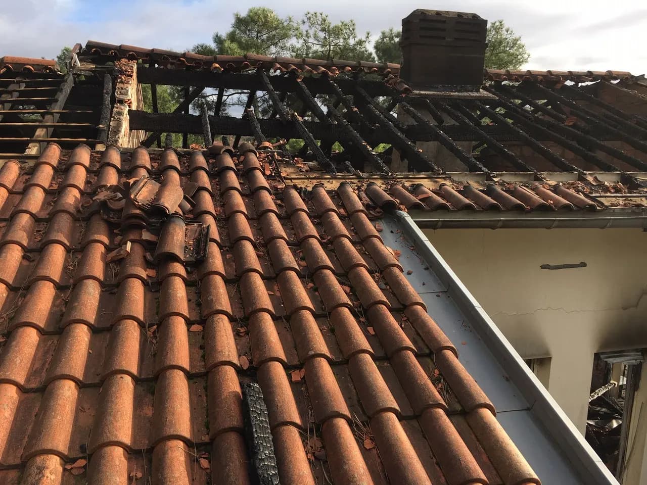 Charpente carbonisée sous une couverture en tuile canal après un incendie