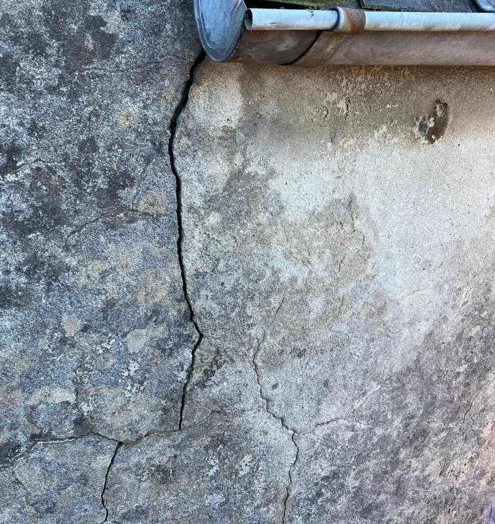 Fissure traversant l'enduit d'un mur sur toute sa hauteur, sous la gouttière et la rive de toiture