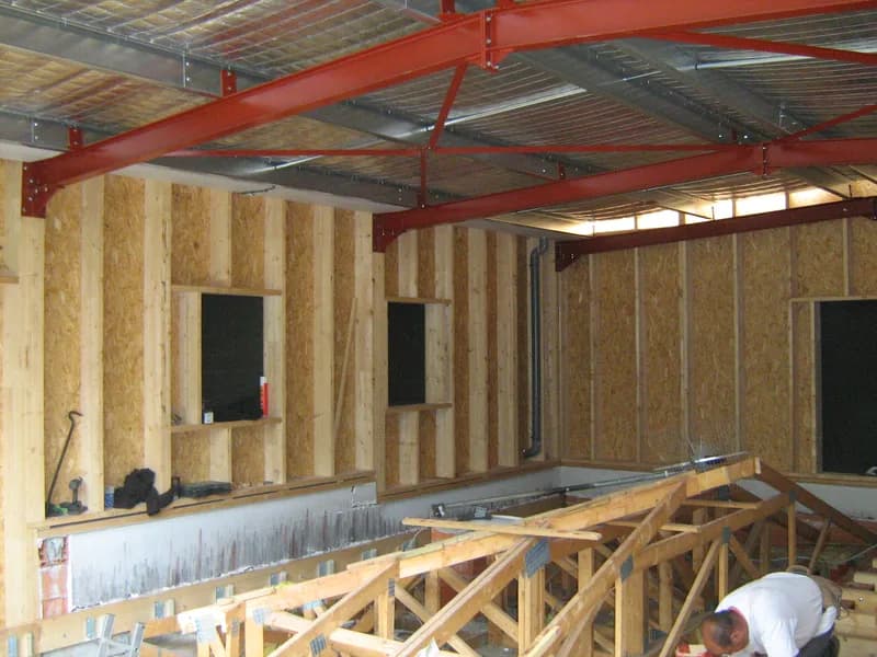 Murs à ossature bois et charpente en cours de montage dans un portique métallique