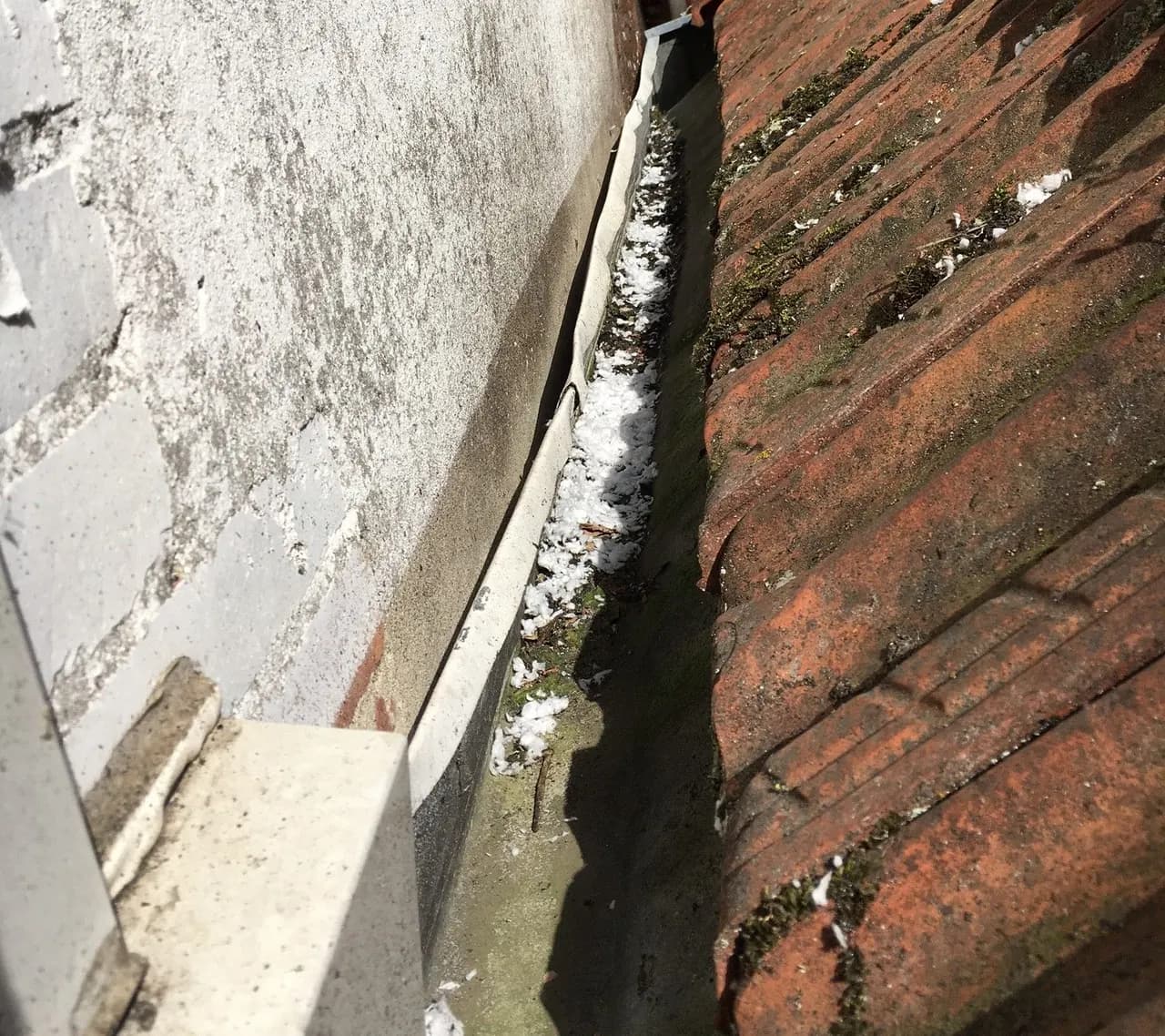 Solin de zinc le long d'un mur, encombré de mousse et de débris à la jonction avec la couverture