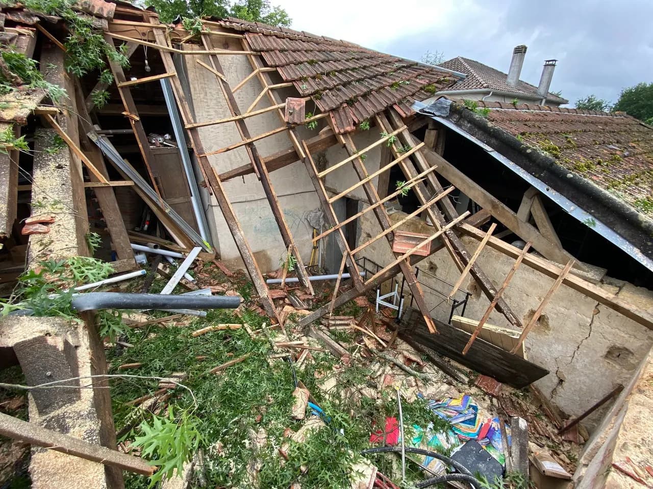Toiture et charpente effondrées après une tempête, tuiles, bois et gravats répandus au sol